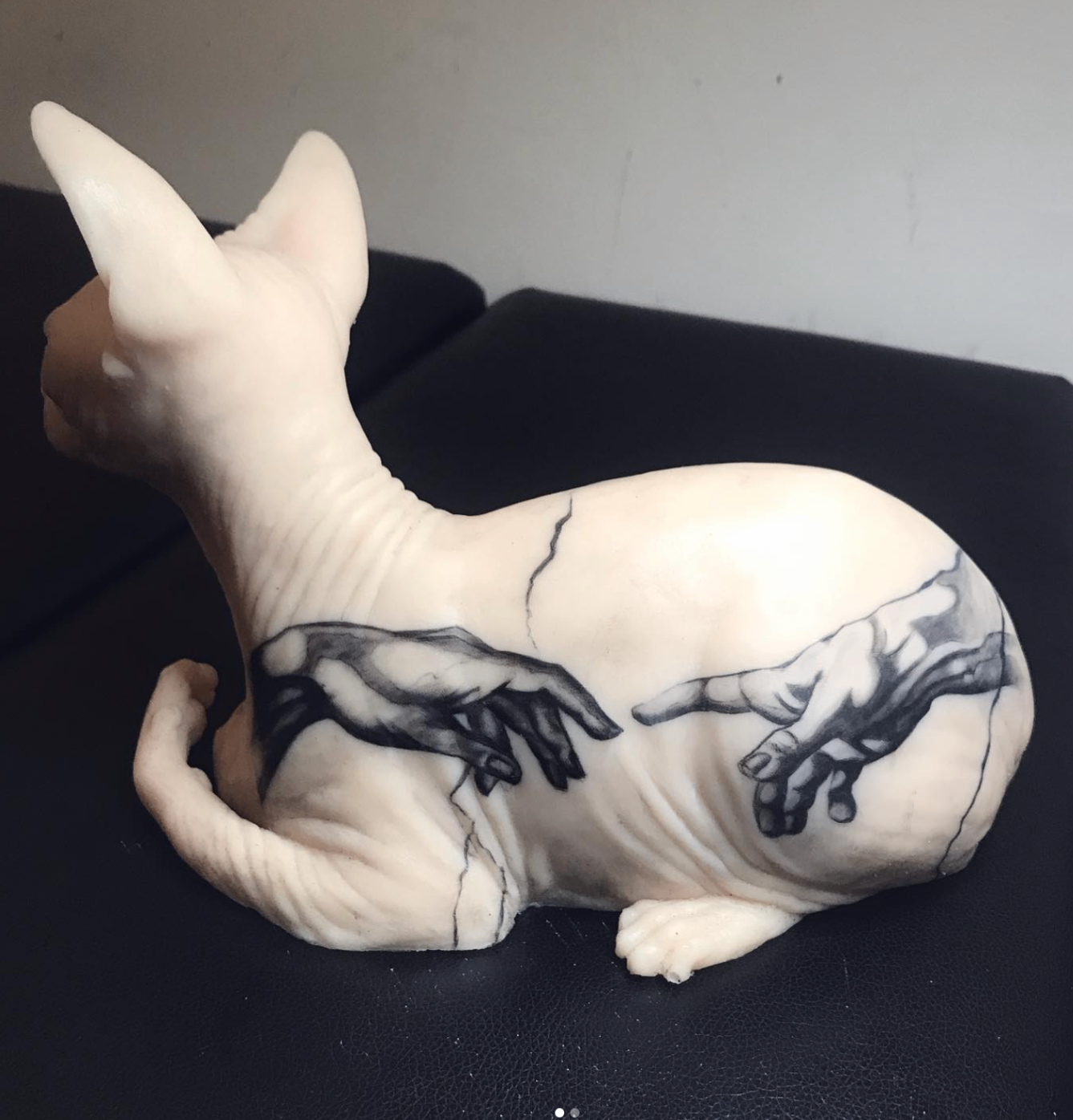 Creation of Adam hands inked on a sphynx cat sculpture